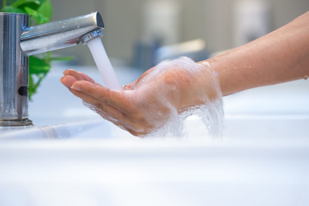 Mão em concha, recebendo um jato de água corrente quente da torneira.