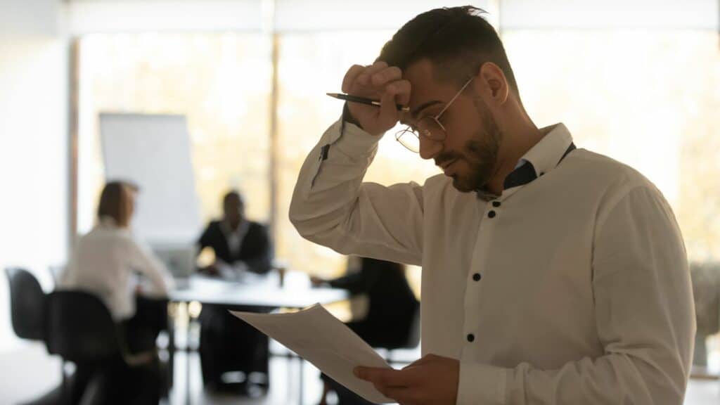 Imagem de um homem vestido de camisa social e um papel e caneta na mão e parece estar preocupado e ansioso para falar