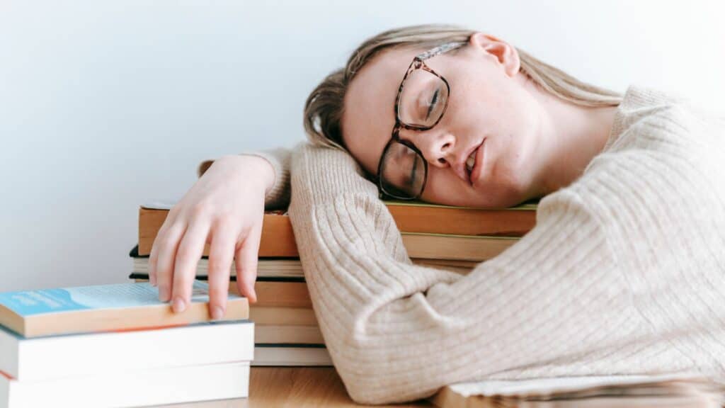 Imagem de uma mulher deitada sobre os livros como se estivesse muito cansada