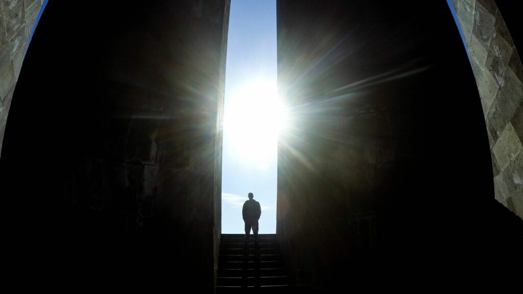 Imagem de um homem no topo de uma escada no meio do que parece a fenda de duas rochas e a luz do sol iluminando o meio