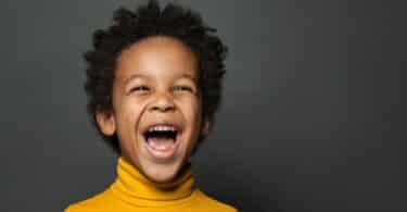 Imagem de um menino negro, pequeno de amarelo sorrindo em um fundo cinza
