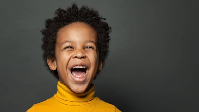 Imagem de um menino negro, pequeno de amarelo sorrindo em um fundo cinza