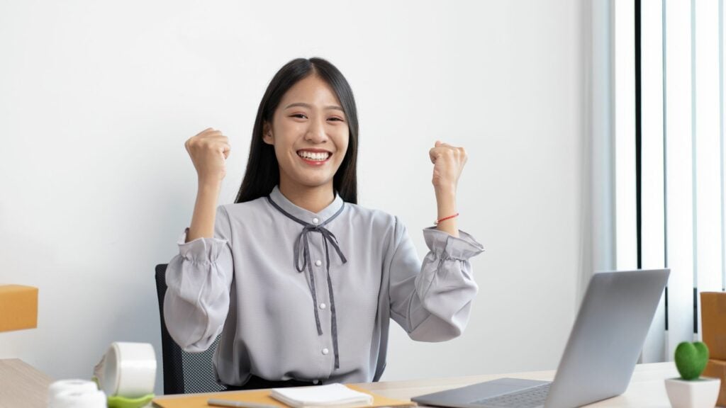 Imagem de uma mulher feliz e com as mãos erguidas como se estivesse tendo sucesso sentada no escritório