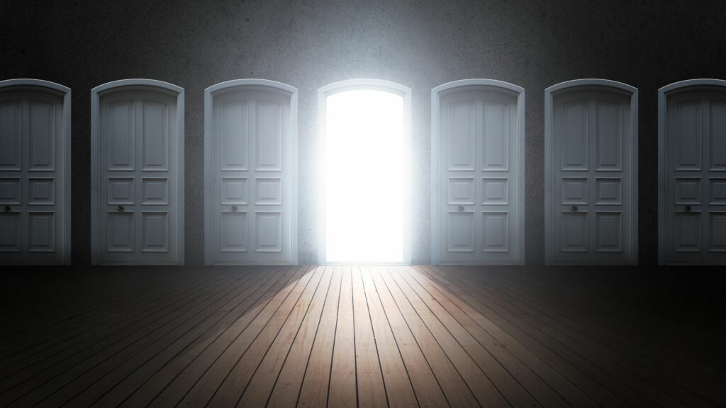 Imagem de uma sala com sete portas, três estão fechadas para um lado e três fechados do o outro e da do meio tem um brilho saindo dela