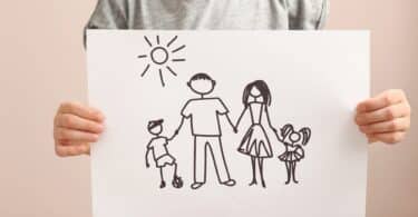 Imagem de uma criança segurando um papel com desenho de família segurando um na mão do outro