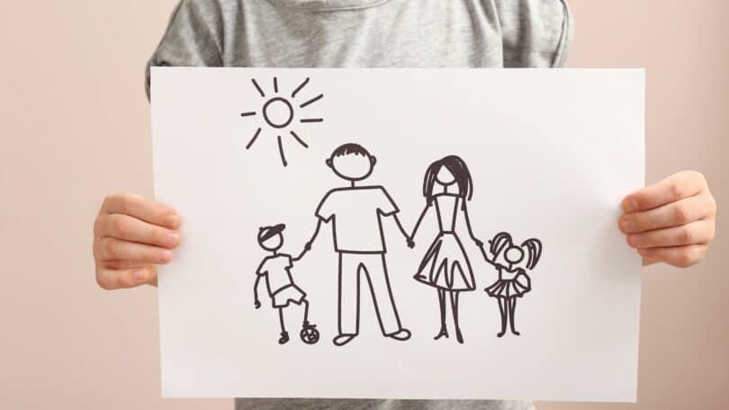Imagem de uma criança segurando um papel com desenho de família segurando um na mão do outro