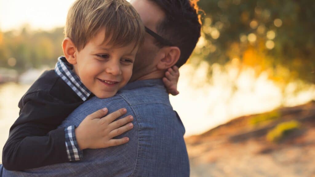 Imagem de um homem abraçando um menino que está sorrindo
