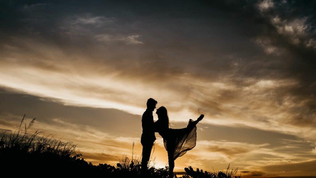Imagem de um casal no campo ao pôr-do-sol, a mulher parece estar dançando