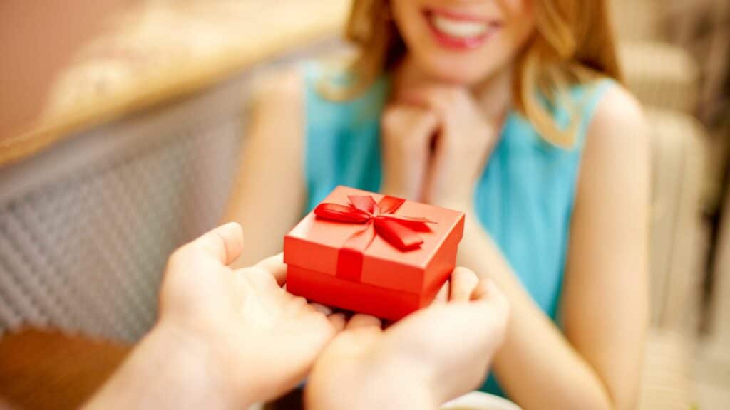 Imagem de uma mulher recebendo uma pequena caixa de presente vermelha e está sorrindo