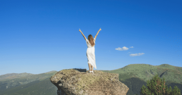 Mulher com os braços abertos em cima de uma rocha