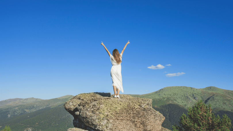 Mulher com os braços abertos em cima de uma rocha