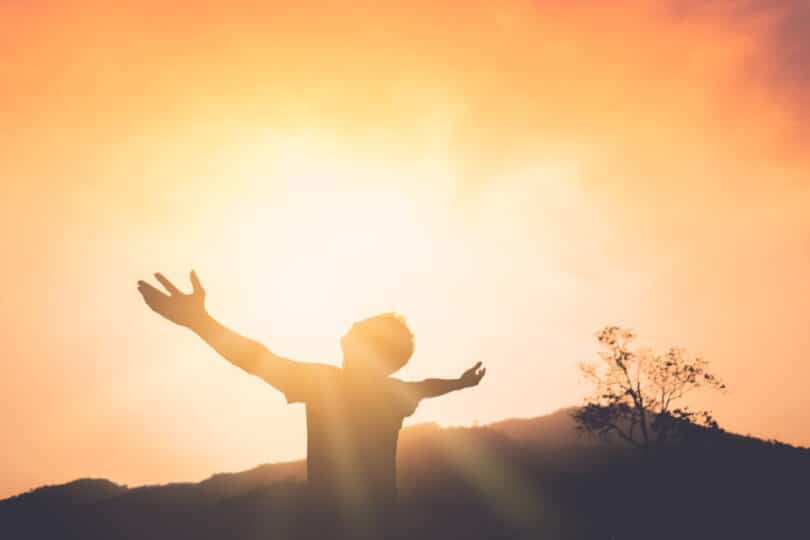 Silhueta de um homem com os braços abertos para o céu no meio da natureza