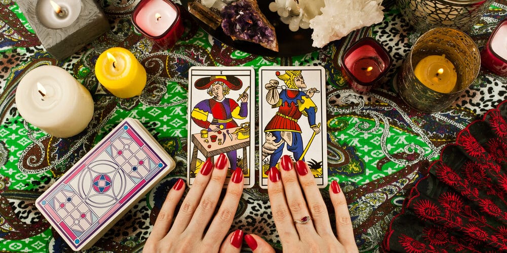 Cartas de tarot de Marselha sobre mesa com velas, ramos de planta, cristais e miçangas