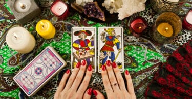 Cartas de tarot de Marselha sobre mesa com velas, ramos de planta, cristais e miçangas