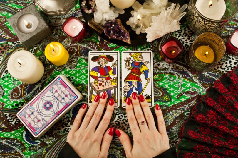 Cartas de tarot de Marselha sobre mesa com velas, ramos de planta, cristais e miçangas