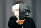 Pessoa anônima segurando duas máscaras diferentes (uma preta e outra branca) na frente de seu rosto