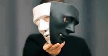Pessoa anônima segurando duas máscaras diferentes (uma preta e outra branca) na frente de seu rosto