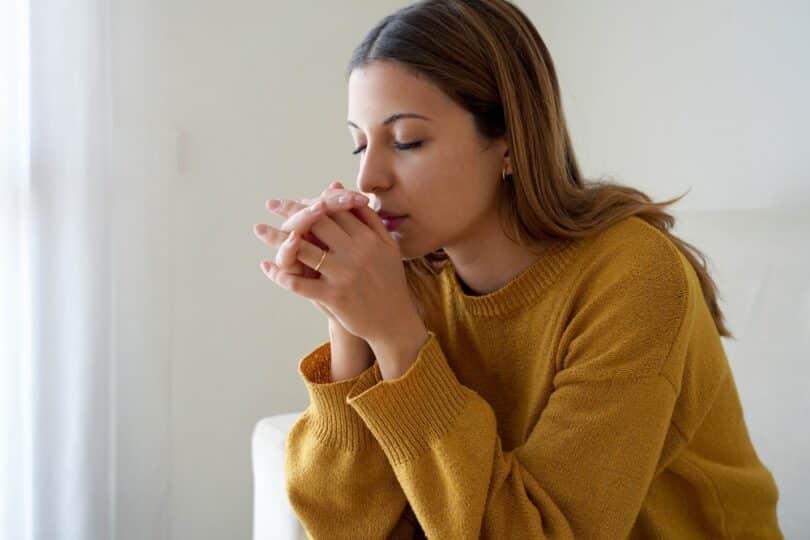 Mulher com as mãos juntas na frente do rosto e os olhos fechados, rezando