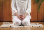 Mulher sentada sobre os calcanhares fazendo Kriya Yoga em ambiente interno
