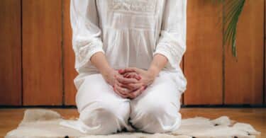 Mulher sentada sobre os calcanhares fazendo Kriya Yoga em ambiente interno