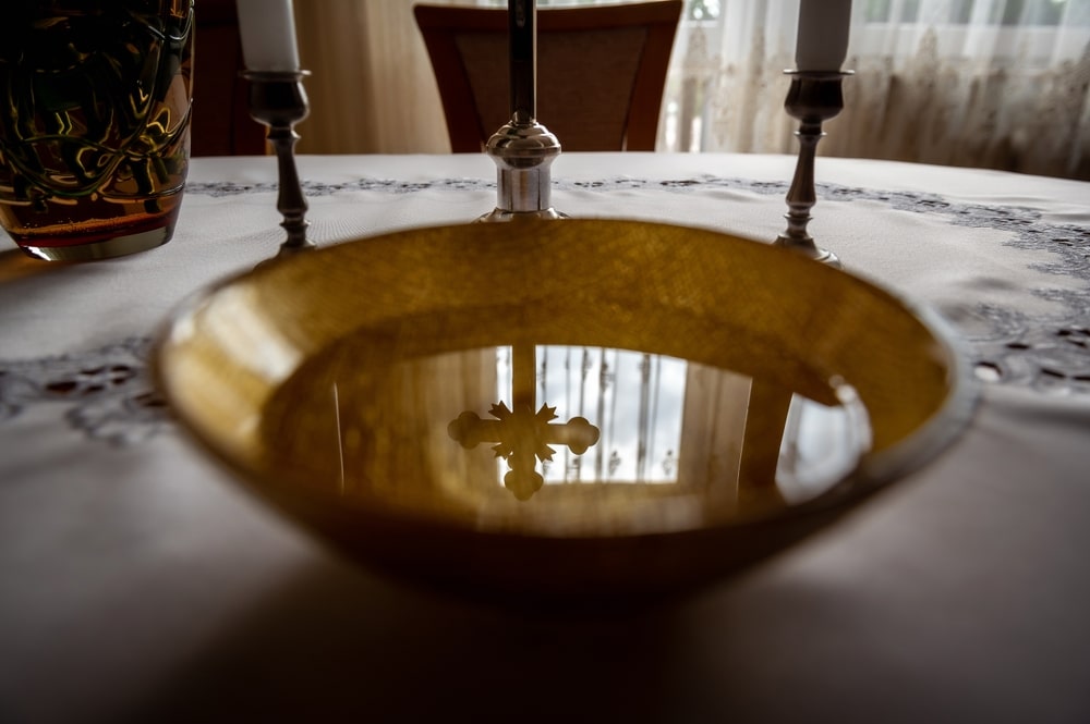 Bacia de água sobre uma mesa com itens religiosos, como velas e símbolos de crucifixo