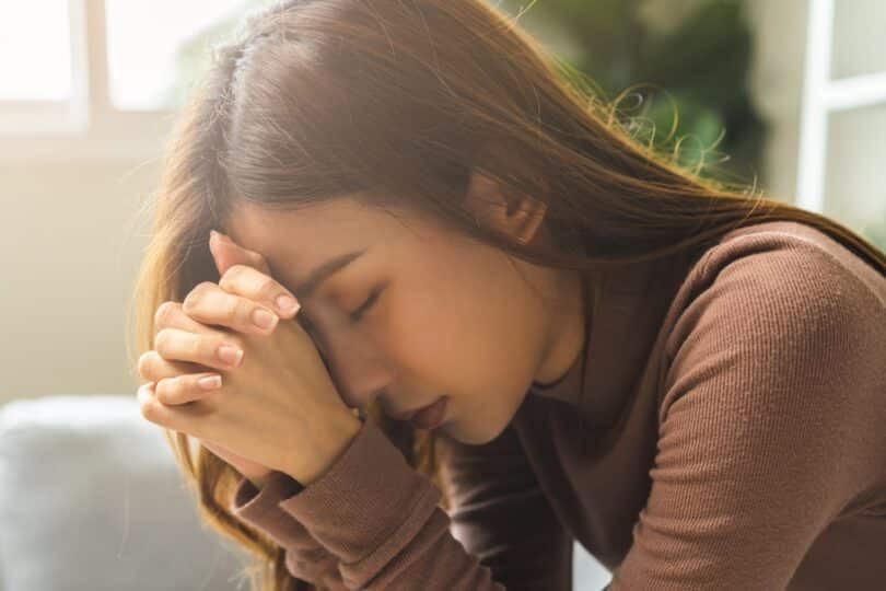 Mulher rezando com as mãos juntas e com os olhos fechados