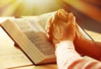 Mãos de pessoa idosa cruzadas sobre uma Bíblia