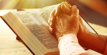 Mãos de pessoa idosa cruzadas sobre uma Bíblia