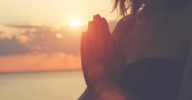 Mulher com as mãos juntas realizando uma oração sob o sol da manhã