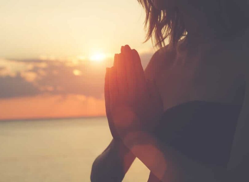 Mulher com as mãos juntas realizando uma oração sob o sol da manhã