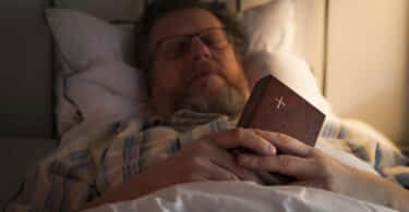 Homem dormindo em sua cama com uma Bíblia na mão