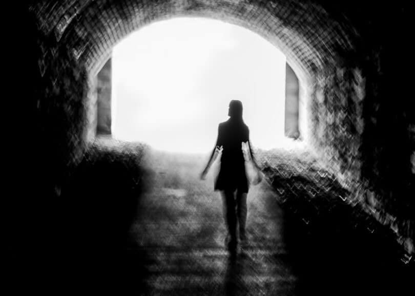Silhueta de uma mulher andando no meio de uma rua escura