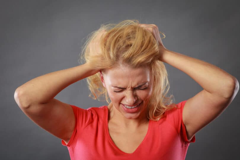 Mulher agoniada, com as mãos atrás do cabelo