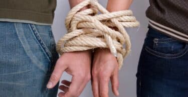 Imagem de duas pessoas com as mãos presas por cordas