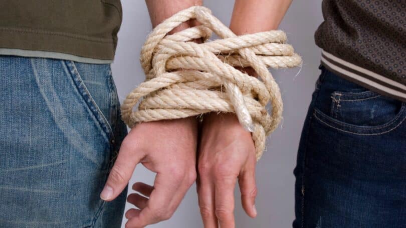 Imagem de duas pessoas com as mãos presas por cordas