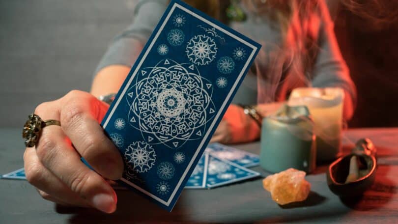 Imagem de uma taróloga segurando uma carta de tarot na mão como se estivesse mostrando para alguém
