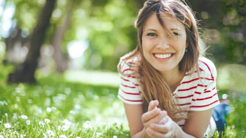 Imagem de uma mulher de bruços em um campo com o rosto para frente e sorrindo