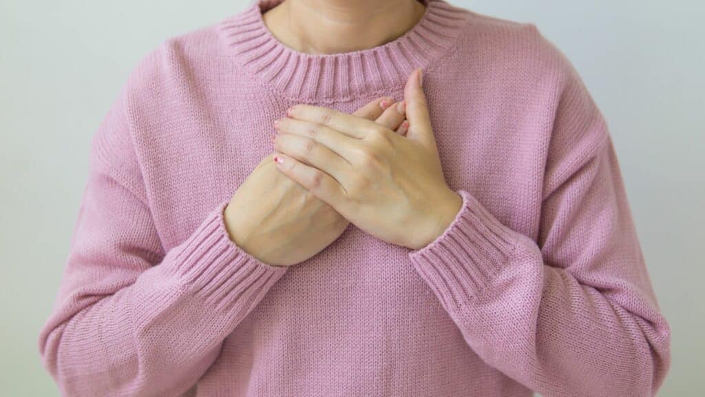 Imagem de uma mulher com uma blusa rosa e as mãos no coração