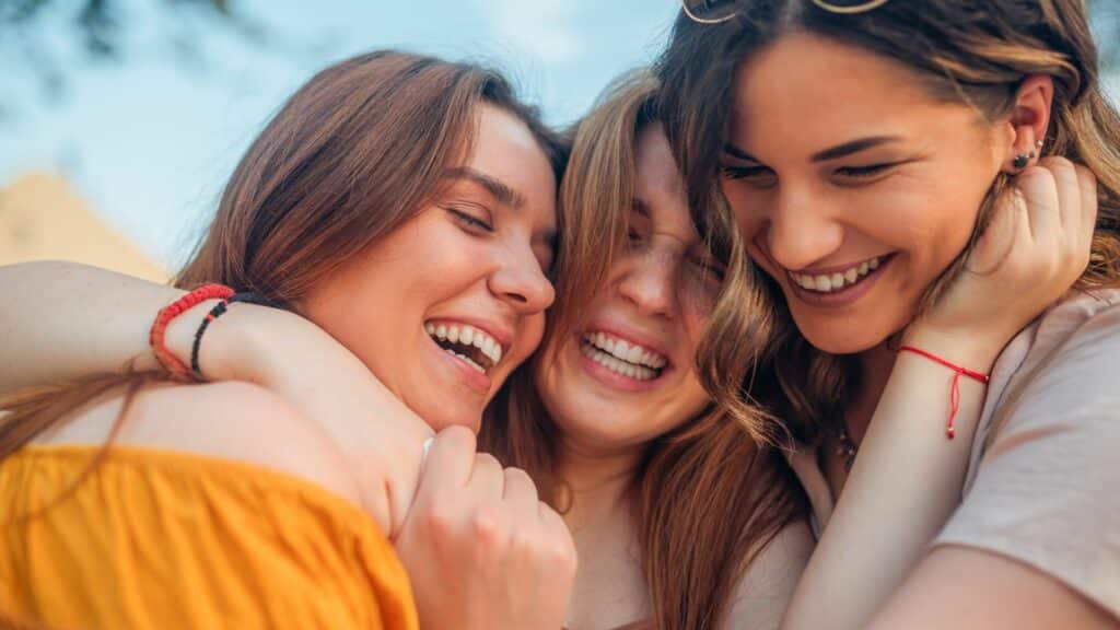 Três amigas se abraçando muito felizes. 