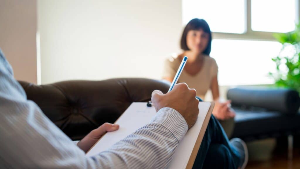 Imagem de um psicólogo fazendo anotações diante de sua paciente