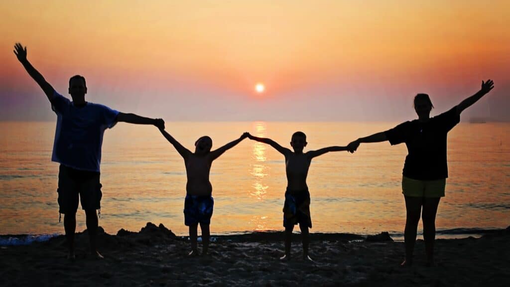 Imagem de uma família de mãos dadas em frente a praia ao pôr-do-sol