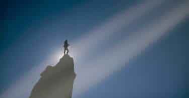 Imagem de um homem em uma montanha bem perto do céu e uma luz vindo em direção a ele