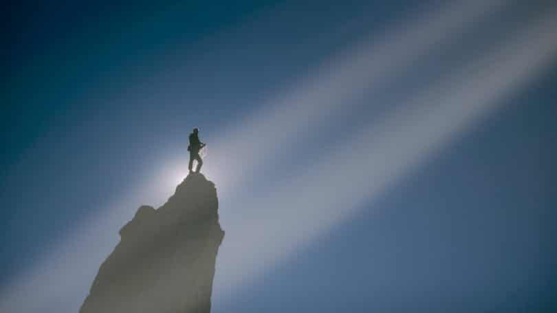 Imagem de um homem em uma montanha bem perto do céu e uma luz vindo em direção a ele