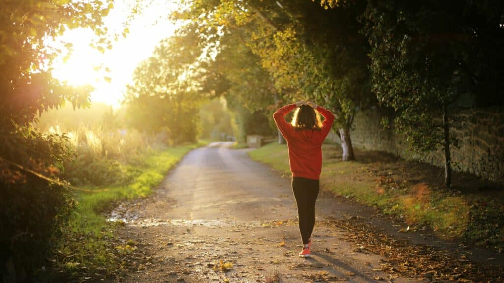 Imagem de uma mulher caminhando em uma estrada com árvores em volta ao final da tarde