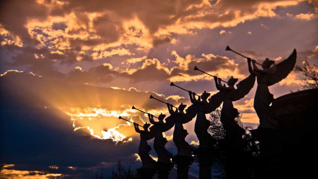 Imagem de estátuas de 6 anjos tocando trombetas e ao fundo o céu alaranjado