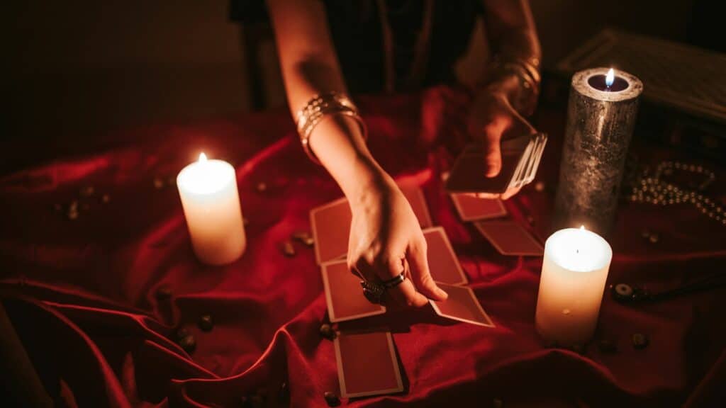 Imagem de uma taróloga fazendo leitura das cartas de tarô, com velas na mesa.