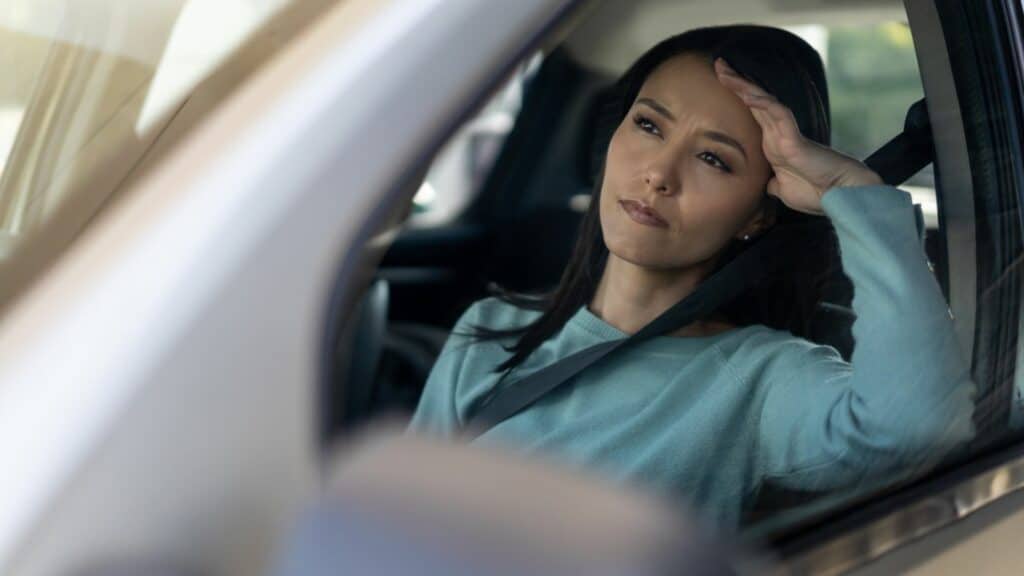 Imagem de uma mulher no carro com semblante de preocupação com a mão na cabeça