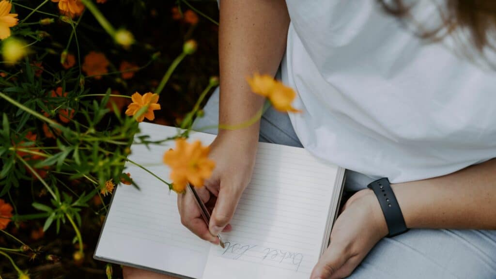 Imagem de uma mulher escrevendo em um caderno, sentada no gramado