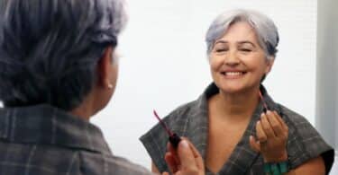 Senhora sorrindo satisfeita para o espelho após fazer sua maquiagem.