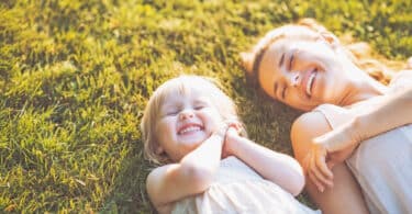 Mulher e sua filha deitadas na grama, sorridentes.